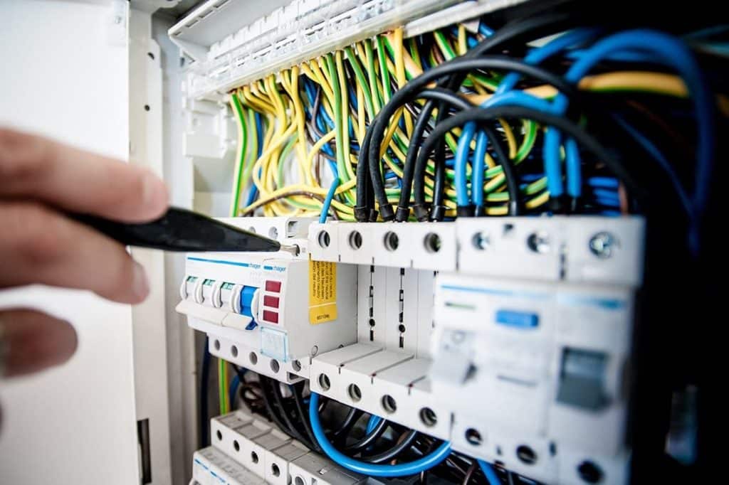 Elektriker arbejder med el-tavle, hvor flere farvede ledninger er tilsluttet forskellige afbrydere og komponenter i el-systemet