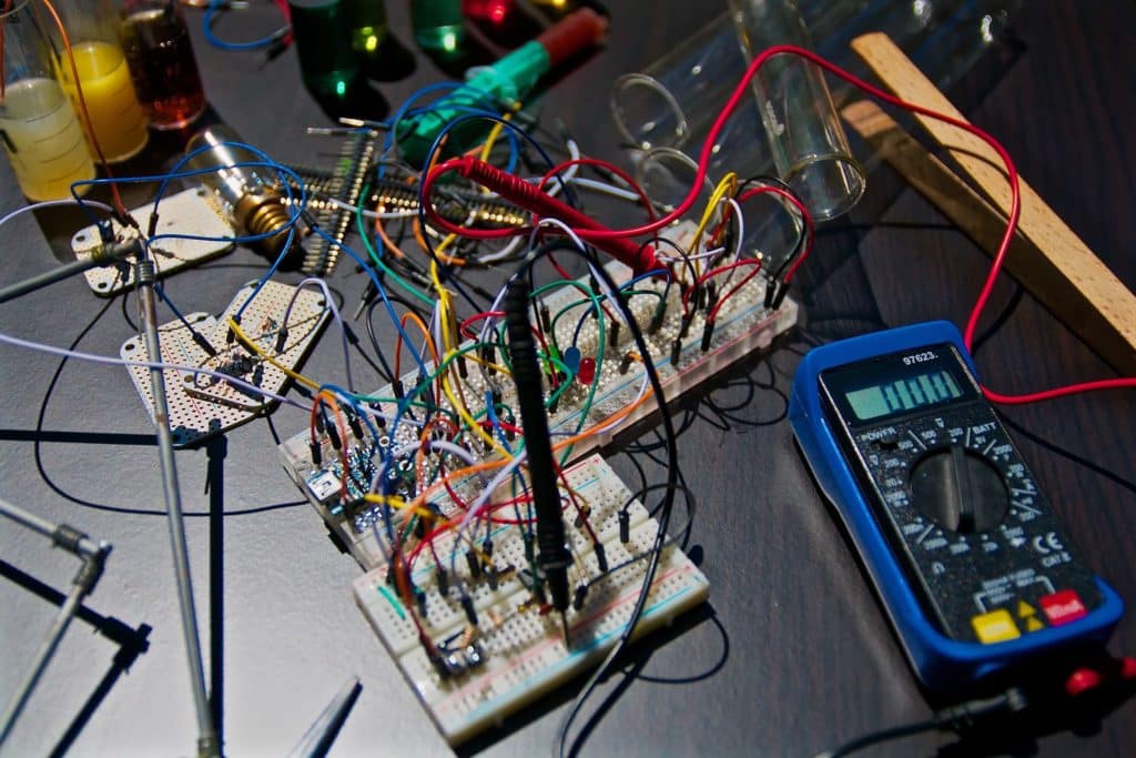 Elektronisk kredsløb med farvede ledninger og måleudstyr på et bord, hvor forskellige komponenter og en digital multimeter er synlige